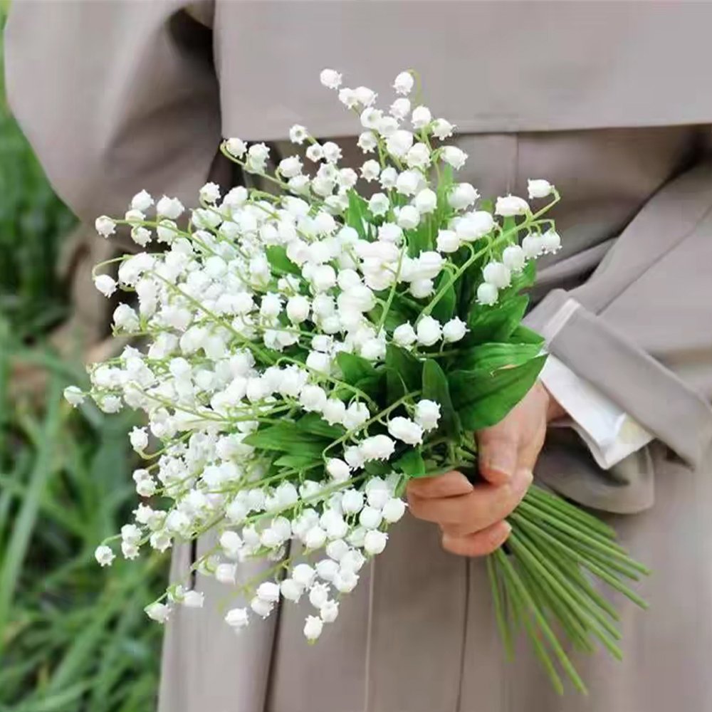Bouquet of artificial white lily of the valley flowers held by a person in a grey coat