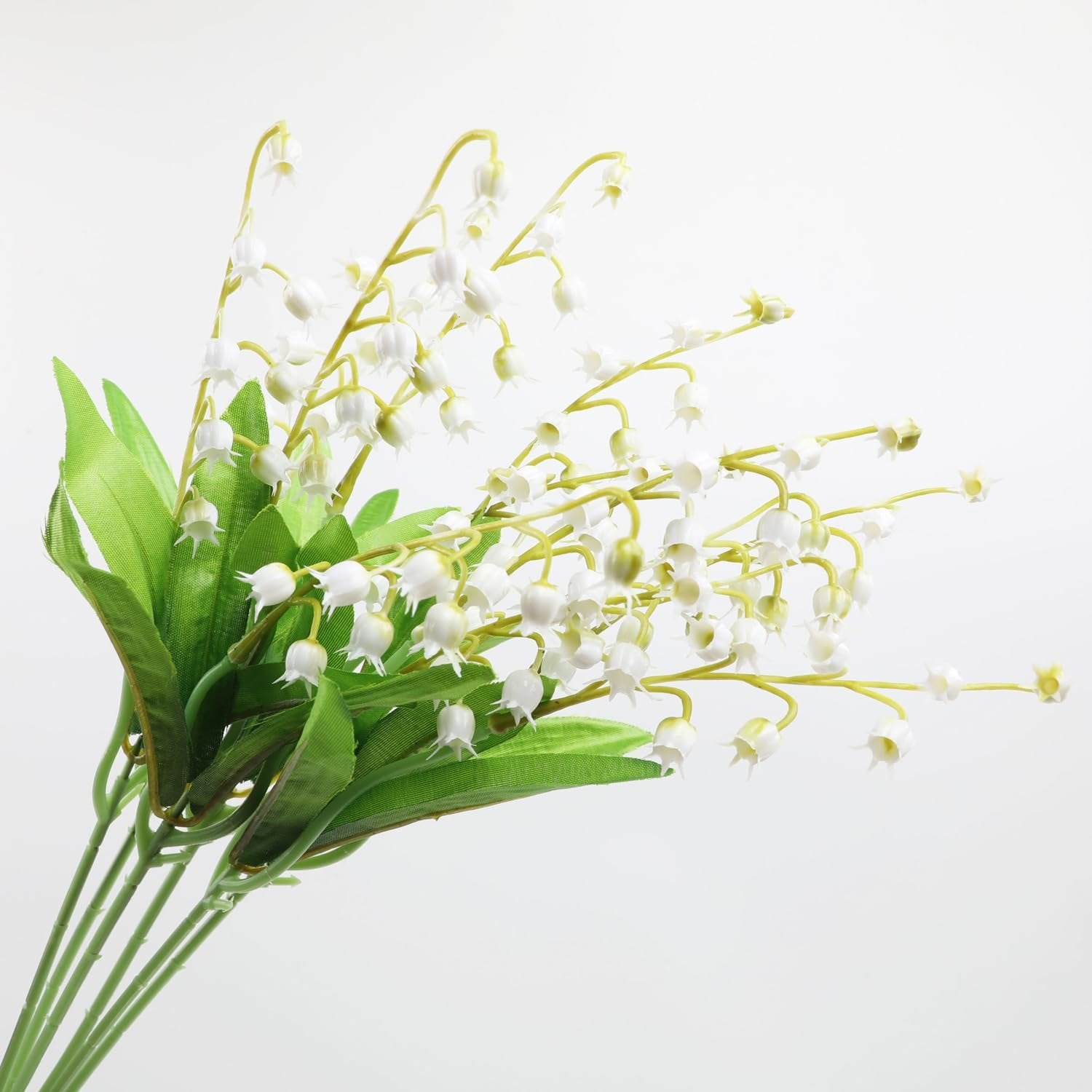 Artificial lily of the valley flowers with green leaves on a white background, close-up view.