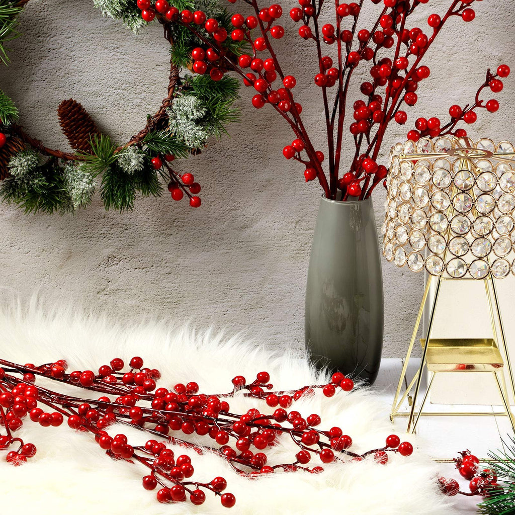 Artificial red berry stems arranged with a Christmas wreath and a decorative lantern on a white fluffy rug.