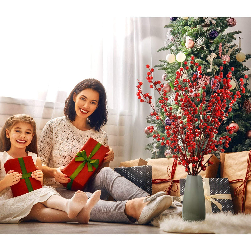 Mother and daughter with Christmas gifts and red berry stems by a decorated tree