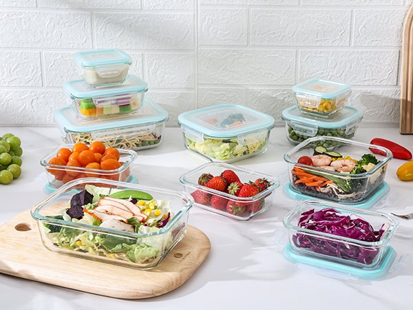 Assortment of glass food storage containers filled with various foods like salad, strawberries, and vegetables, arranged on a countertop.