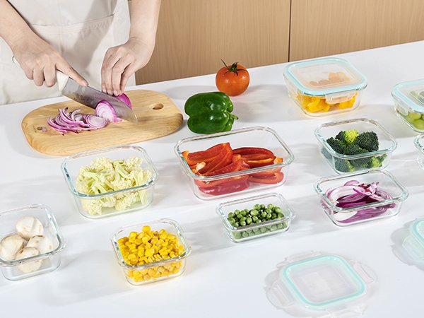 Glass food storage containers filled with various vegetables and mushrooms, with a person slicing red onion in the background.