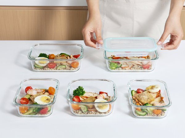 Glass food storage containers filled with meal prep, one lid being closed by hands.