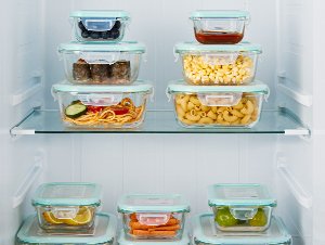 Assortment of glass food storage containers filled with various foods, neatly arranged on refrigerator shelves.
