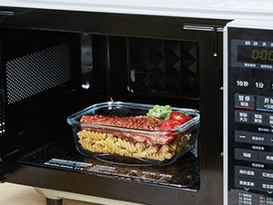 Rectangular glass food storage container with pasta and salad inside, placed in a microwave.