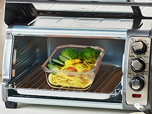 Glass food container with pasta, broccoli, and tomatoes inside a toaster oven