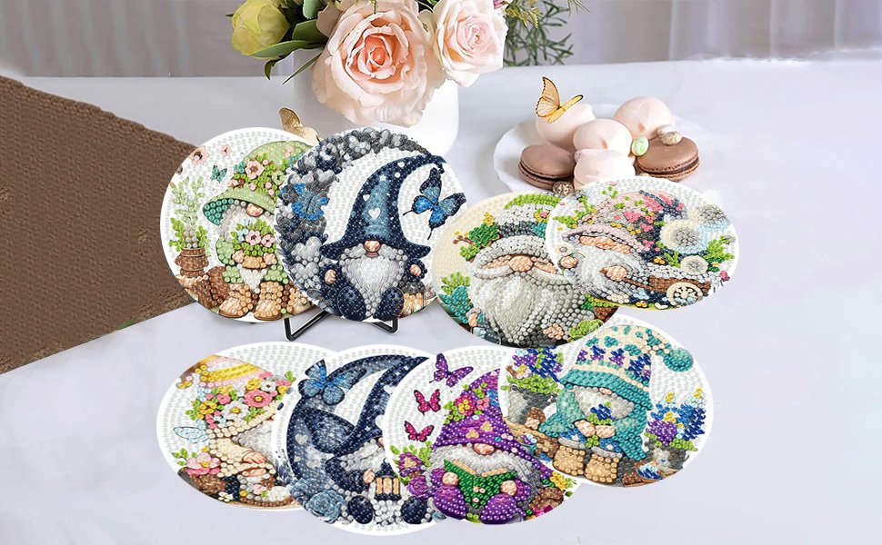 Eight diamond art coaster kits featuring gnomes and butterflies, displayed on a table with flowers and macarons.