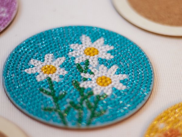 Diamond art coaster with three white daisies on a teal background, close-up view.