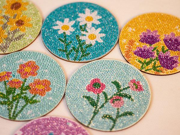 Diamond art coasters with flower designs, including sunflowers, daisies, and other floral patterns, arranged on a white surface.