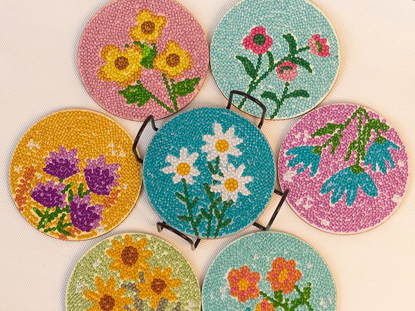 Diamond art coasters with flower designs displayed on a black metal holder