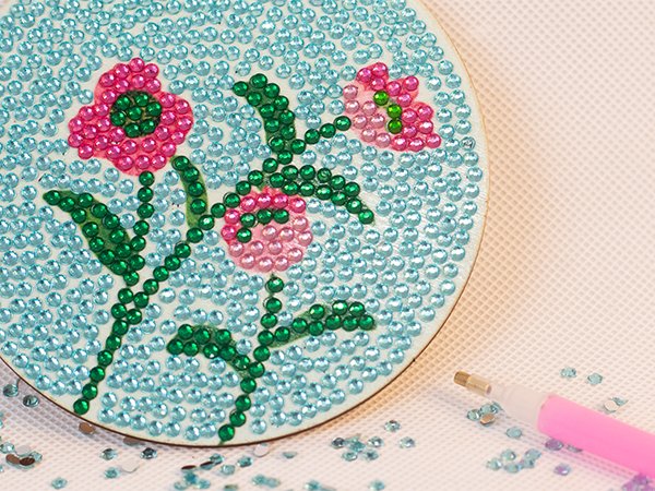 Diamond art coaster kit with pink and green flower design, showing a partially completed coaster and a pink applicator tool.