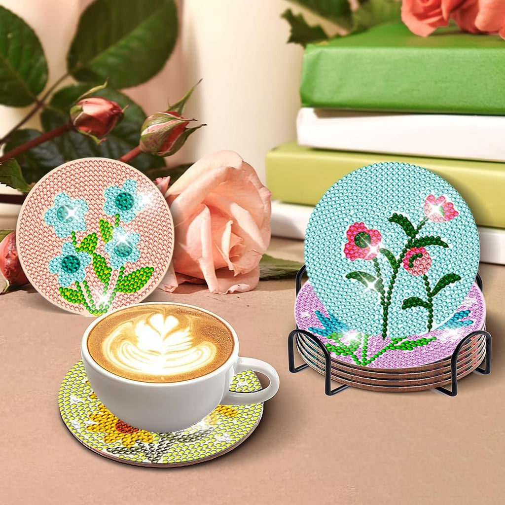 Diamond art coasters with flower designs in a holder next to a coffee cup and roses