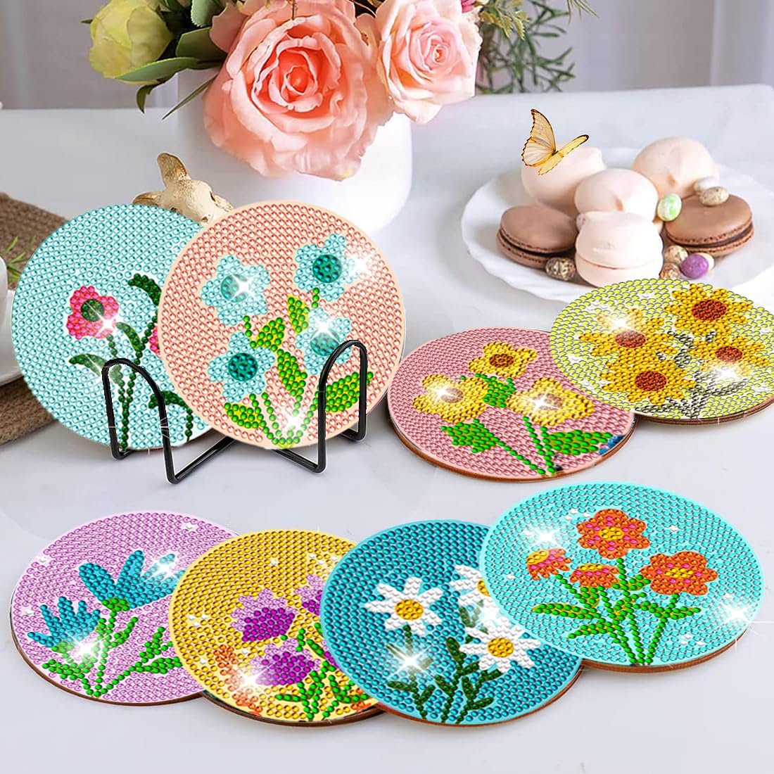 Diamond art coasters with floral designs displayed on a table with macarons and flowers