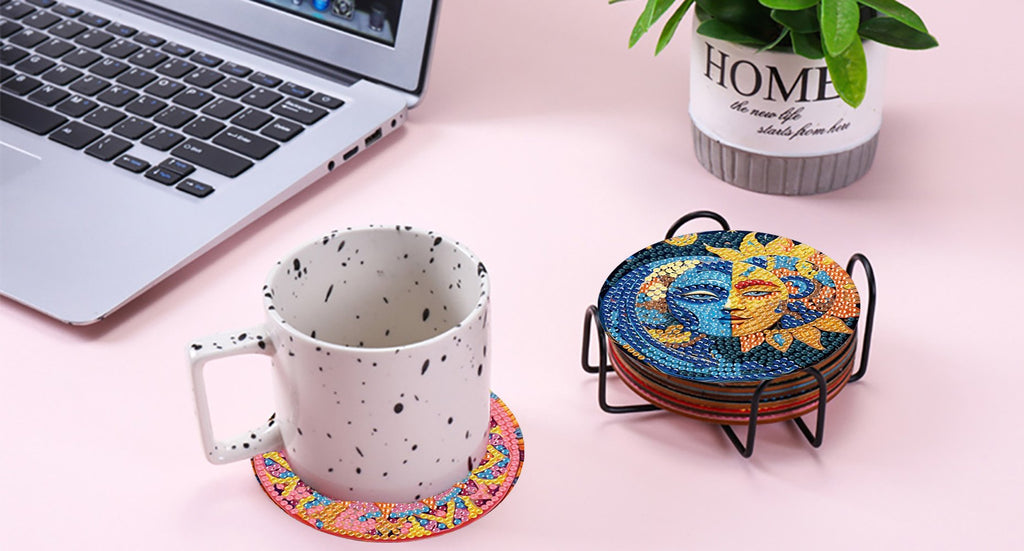 Diamond art coasters with sun and moon designs in a holder next to a mug and laptop