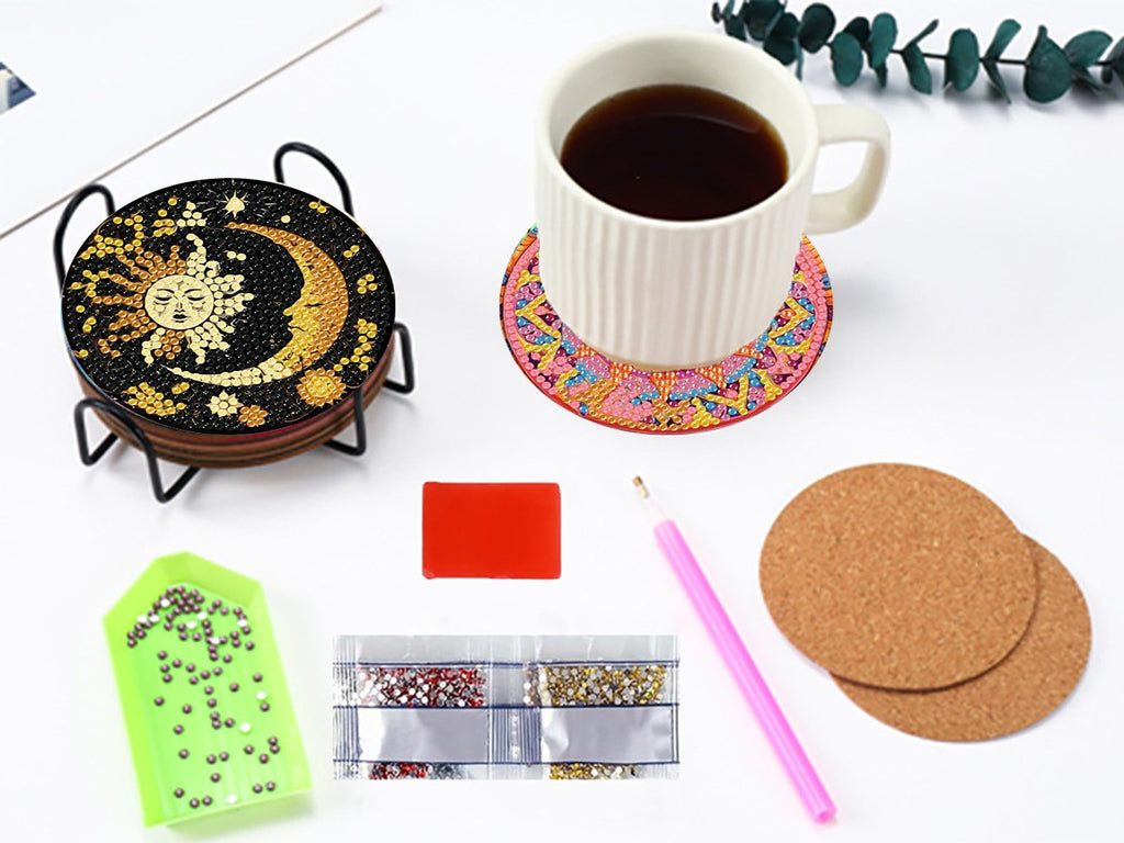 Diamond art coaster kit with sun and moon design, cup, diamond tray, tool, and cork pads on a white surface.