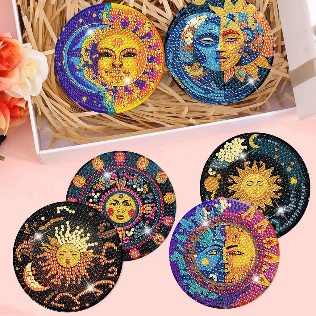 Diamond art coasters with sun and moon designs arranged in a box with straw and flowers.