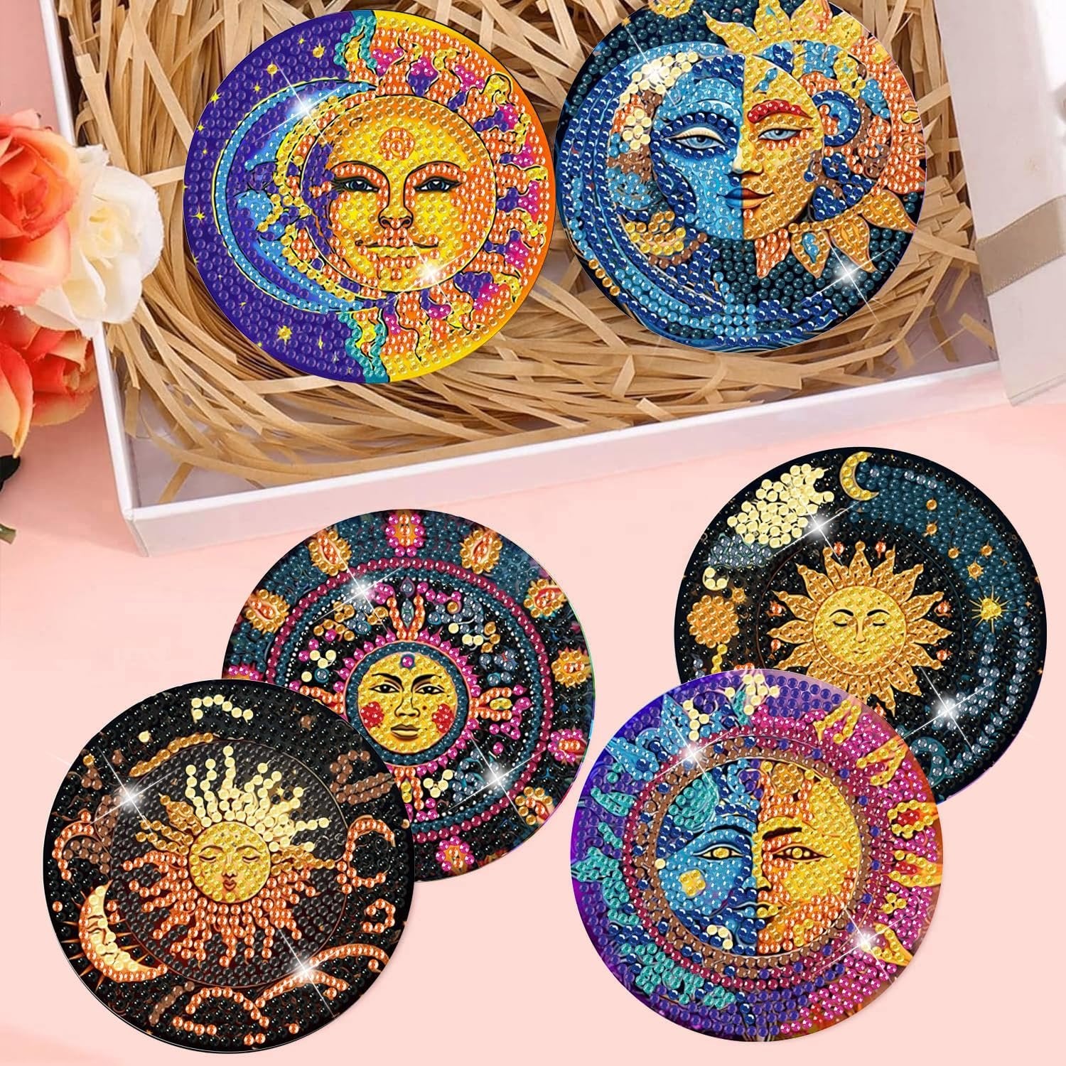Diamond art coasters with sun and moon designs arranged in a box with straw and flowers.