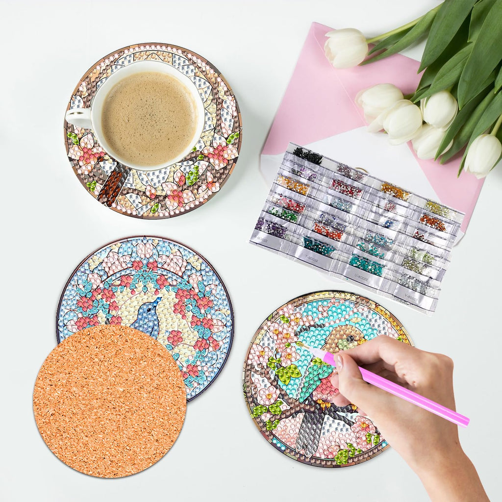 Diamond painting coasters kit with coffee cup, cork base, and diamond beads laid out on a white surface with tulips and pink envelope.