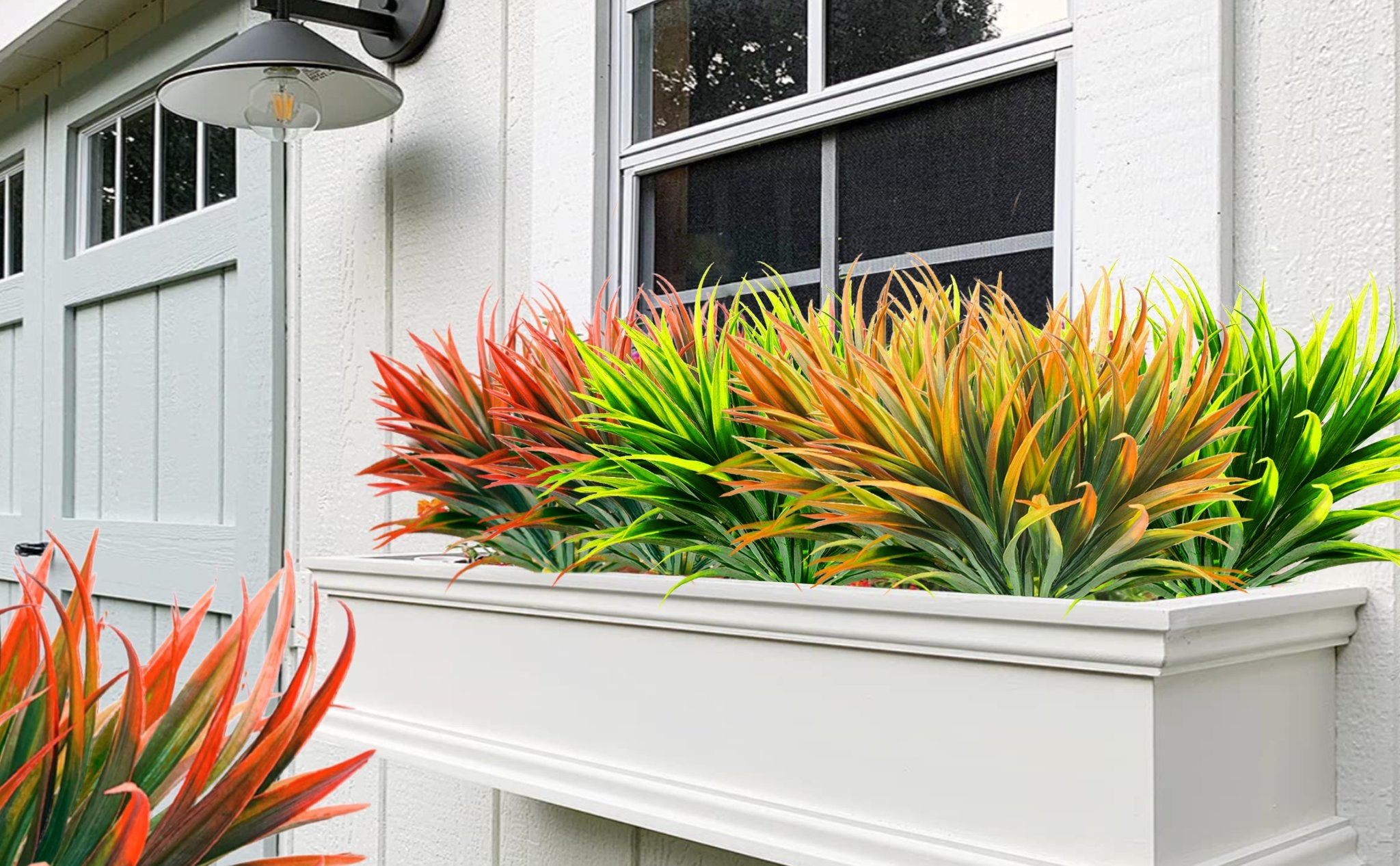 Artificial tall grass plants in a white window planter box against a white wall and window.