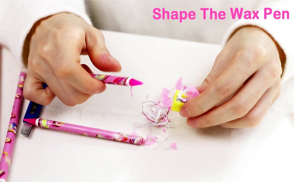 Hands sharpening a pink rhinestone picker wax pencil with a yellow sharpener, shavings on a white surface.