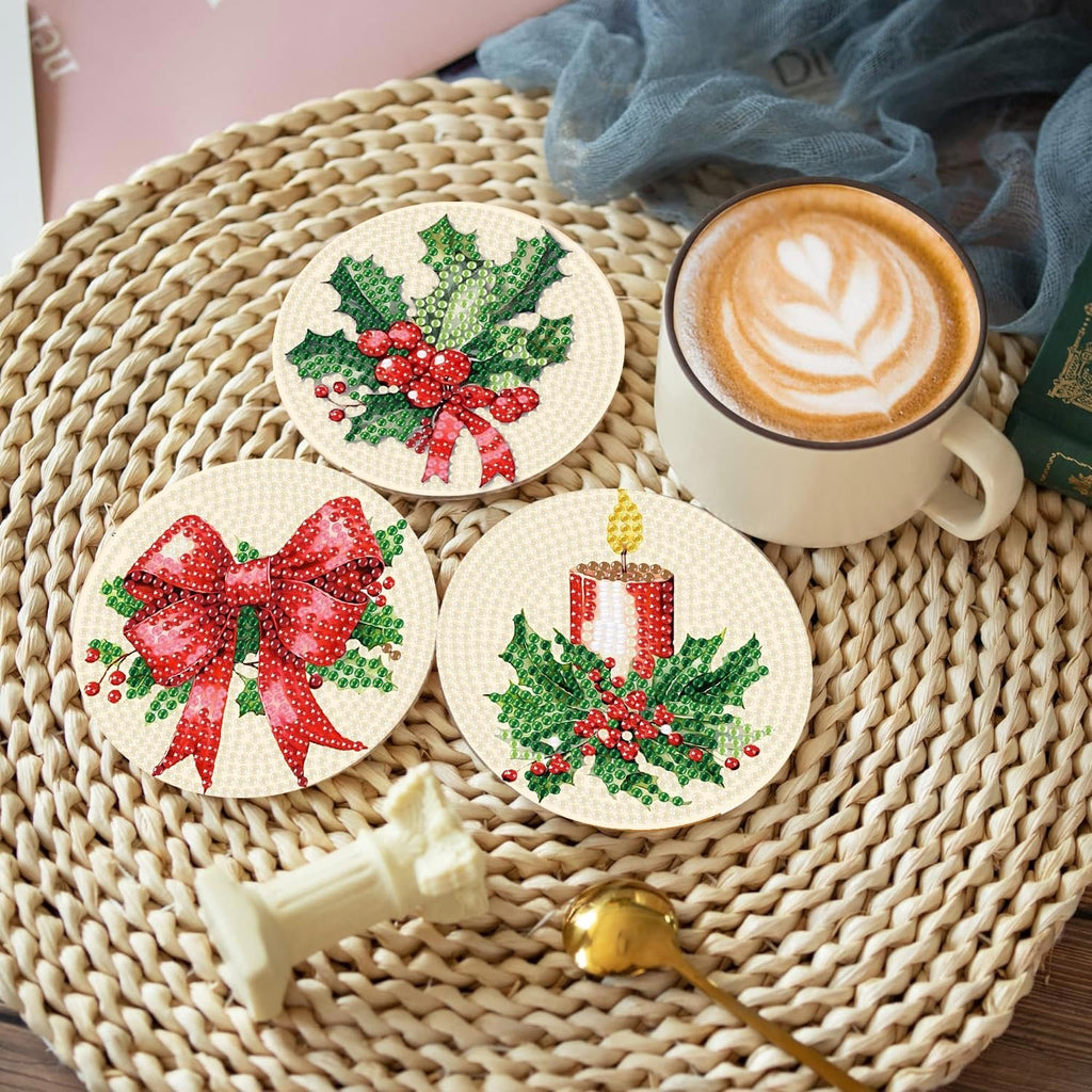 Three Christmas diamond painting coasters with holly, bow, and candle designs, next to a coffee cup.