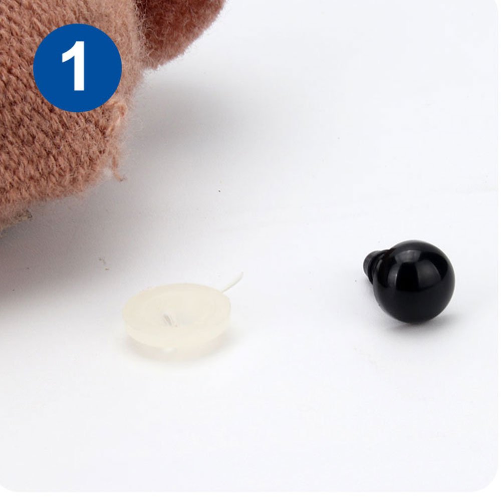 Close-up of a black plastic safety eye and a white washer on a white background, with a fuzzy brown material in the upper left corner.