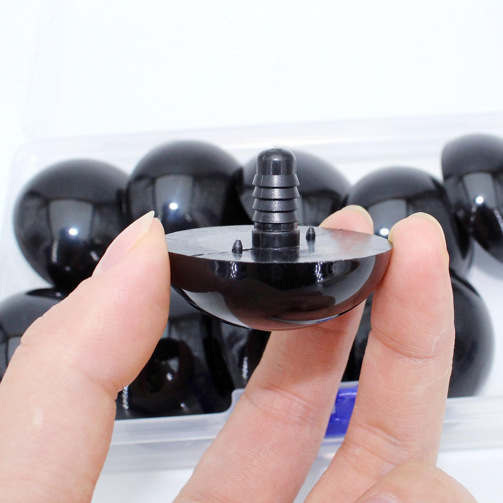 Close-up of a hand holding a black safety eye with a plastic washer stem, showing a row of similar eyes in a clear container.