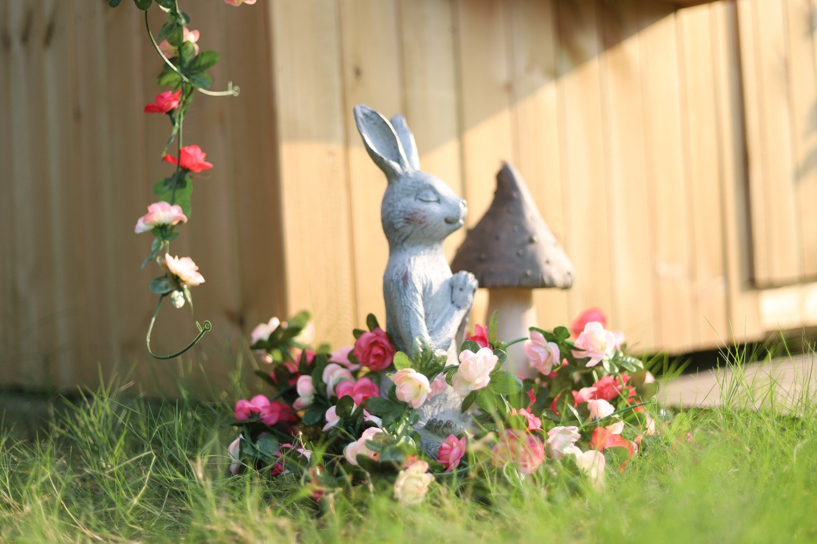 Artificial pink and red rose flower garland draped around a garden statue of a rabbit and mushroom.