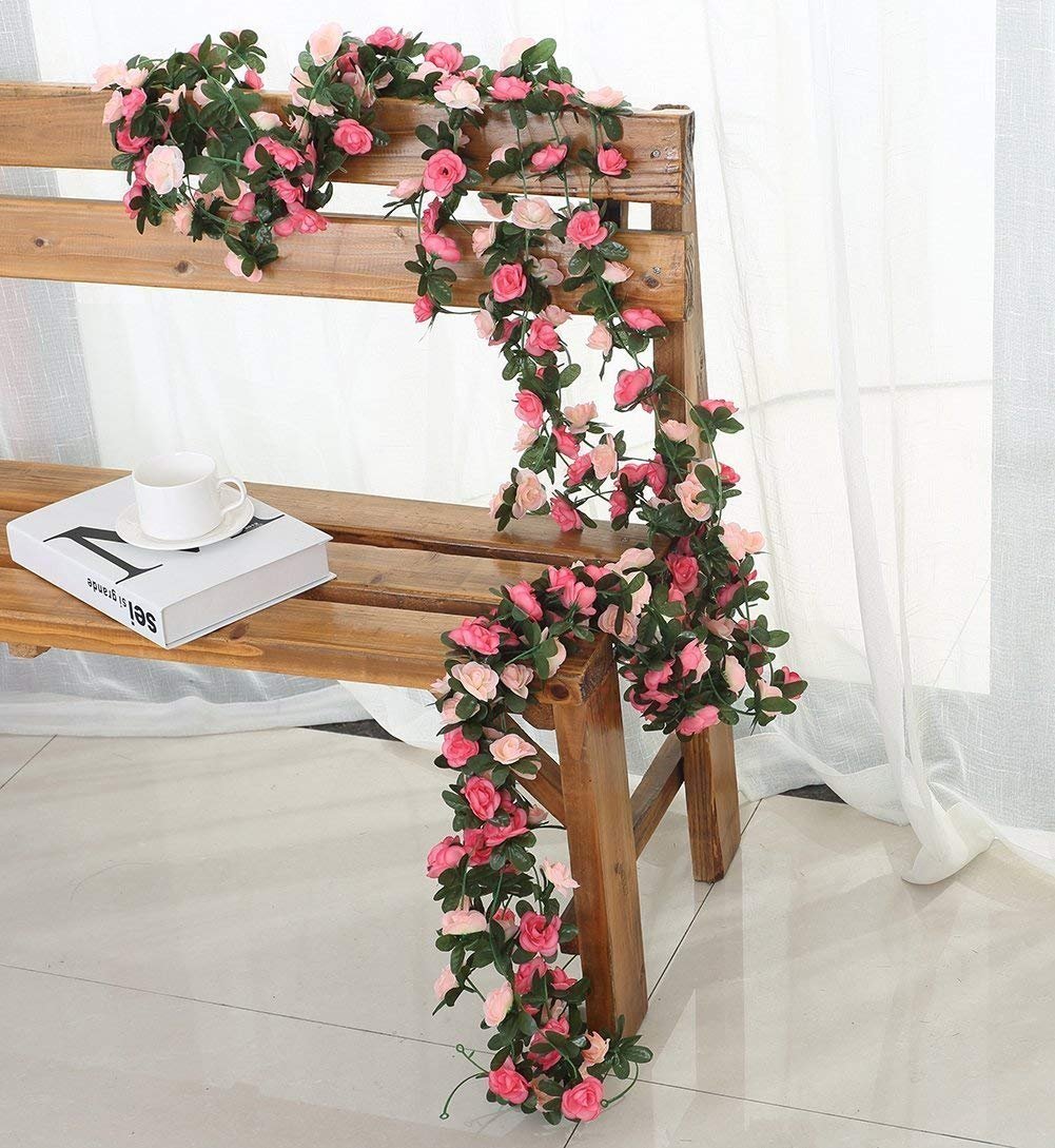 Pink and light pink rose flower garland draped over a wooden bench with a book and cup