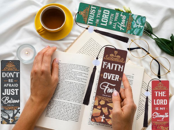 Diamond art bookmarks with Bible verses and tassels laid on an open book next to a cup of tea.
