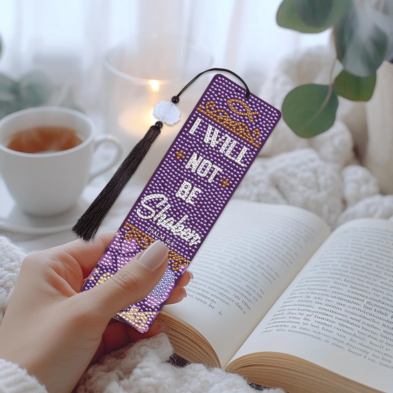 Diamond art bookmark with Bible verse 'I will not be shaken' and tassel, held by a hand over an open book.