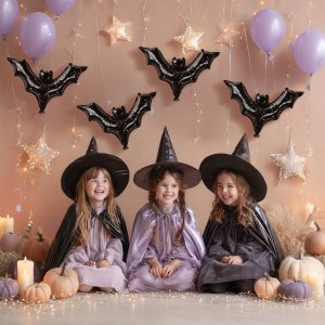 Three smiling children in witch costumes sit in front of black bat balloons and purple balloons, with pumpkins and star lights.