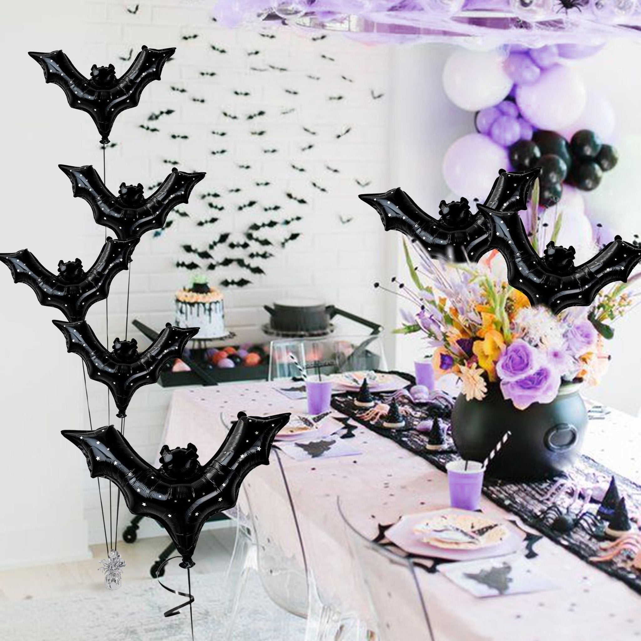 Black bat foil balloons with star pattern floating above a Halloween party table setting