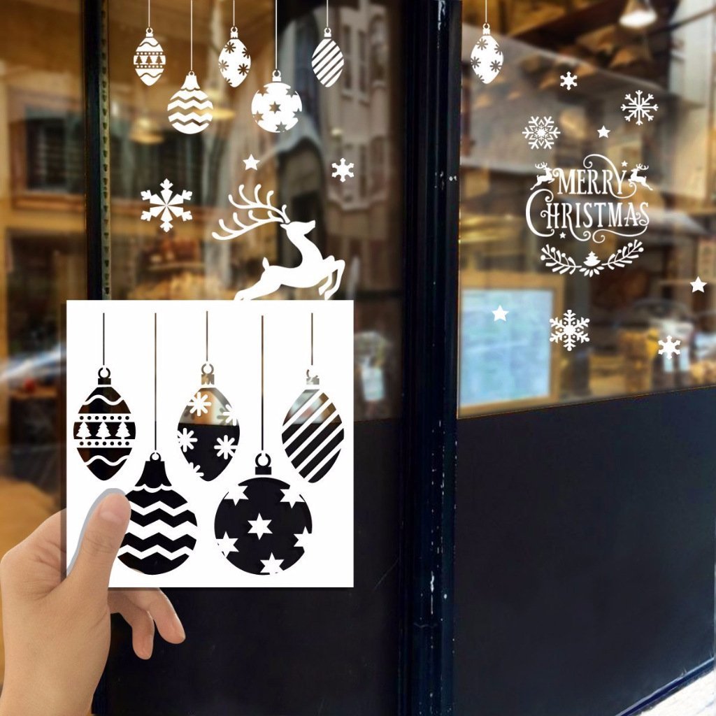 Hand holding a Christmas stencil set with ornaments, snowflakes, and a reindeer applied to a window.