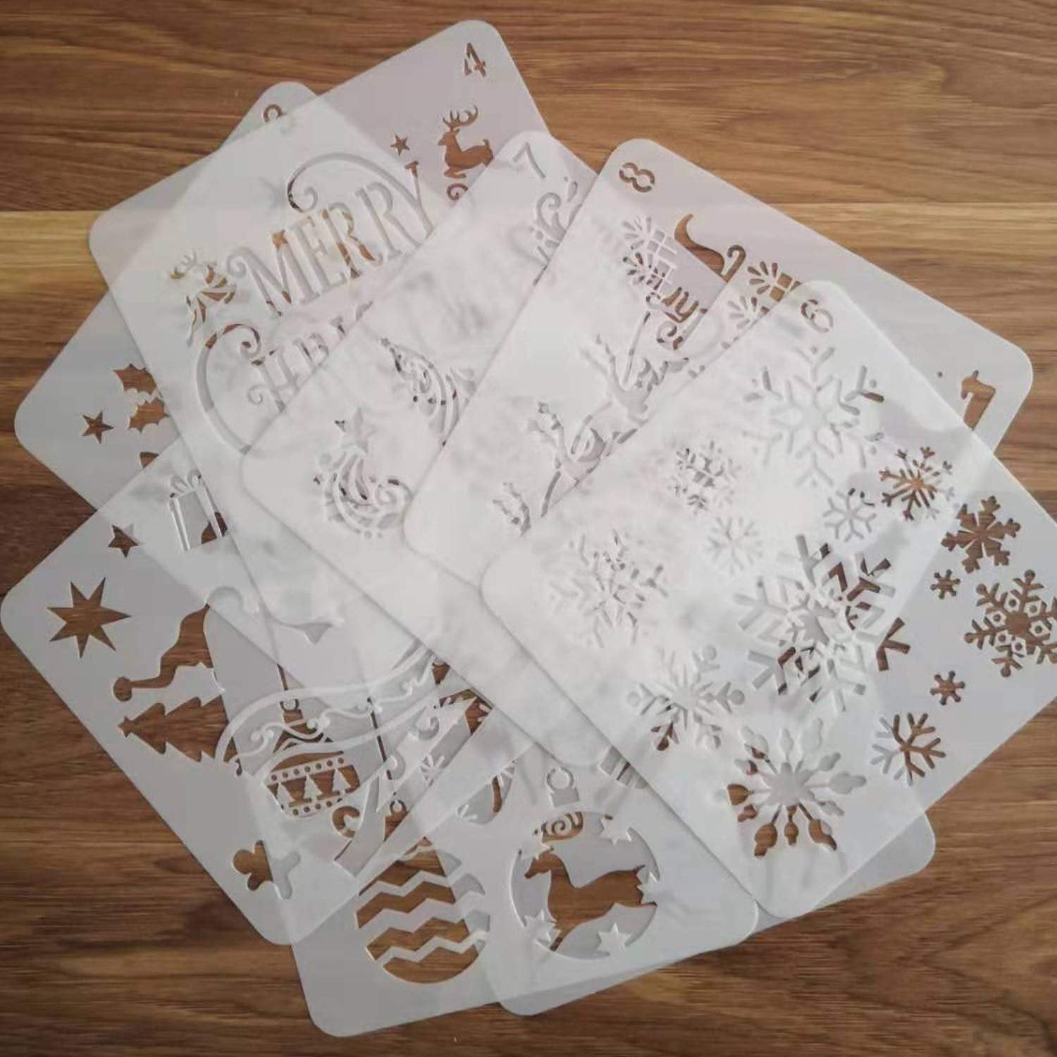 Set of 8 white plastic Christmas stencils with holiday designs like snowflakes, reindeer, and trees, fanned out on a wooden surface.