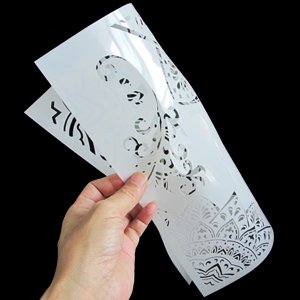 Hand holding two reusable PET stencils with intricate floral and mandala patterns against a black background.