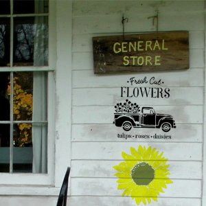 Farm theme stencils applied to a white wooden wall, showing a vintage truck with flowers, a sunflower, and text.