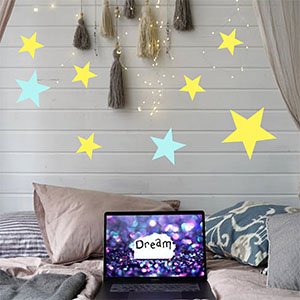 Various sized yellow and blue star cutouts on a white paneled wall above a bed with a laptop displaying the word 'Dream'.