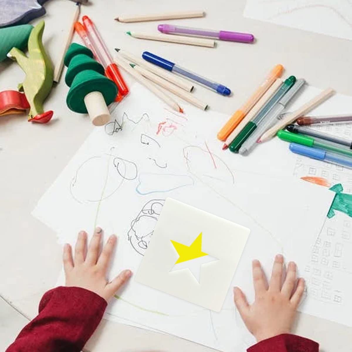 Child's hands on a table with drawing paper, colored pencils, and a star stencil.
