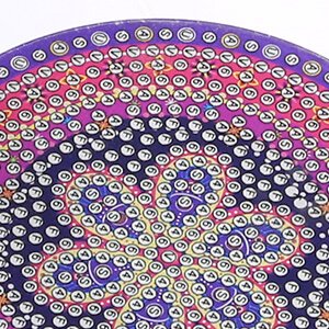 Close-up of a round diamond painting coaster with a purple and yellow mandala pattern, showing small numbered and lettered beads.