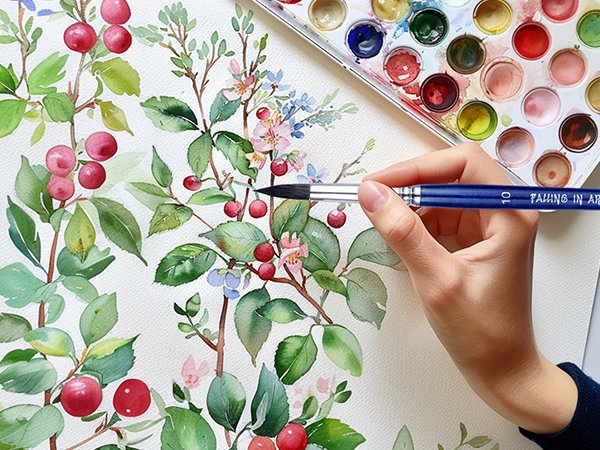 Hand holding a paintbrush with '' logo, painting a floral design with a watercolor palette