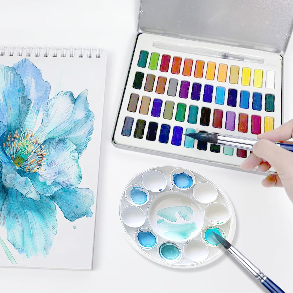 Watercolor painting set with a palette, brushes, and a watercolor painting of a blue flower on a sketchbook.