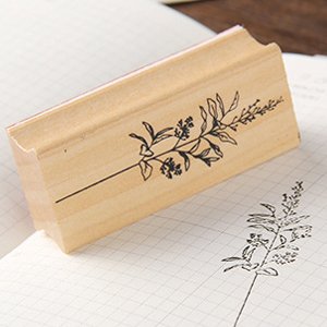 Wooden rubber stamp with a delicate floral branch design, shown on a grid paper background with a stamped impression.