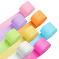 Eight rolls of crepe paper streamers in pastel and bright colors arranged diagonally on a white background.