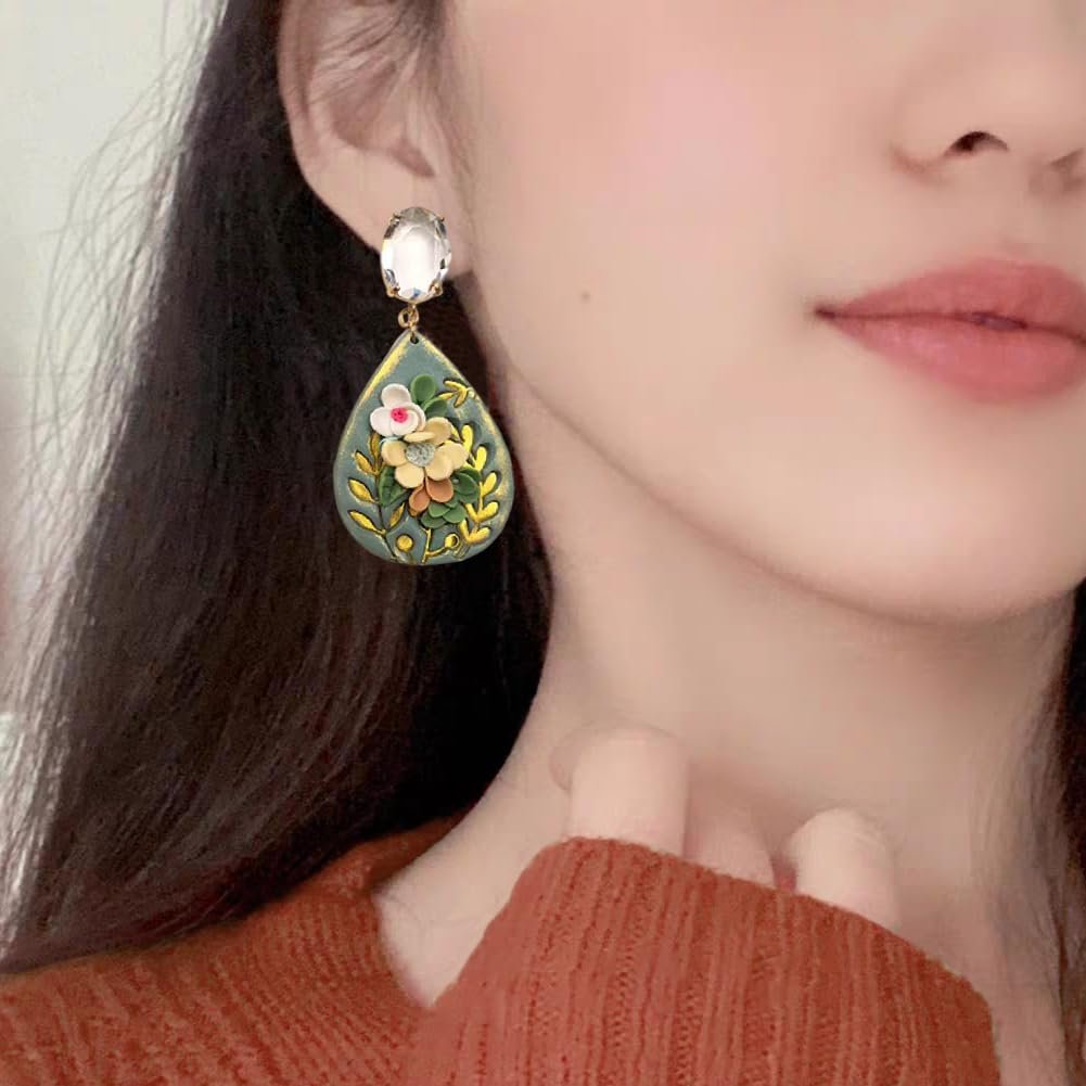 Close-up of a woman wearing teardrop-shaped botanical earrings with floral designs and clear gemstones.