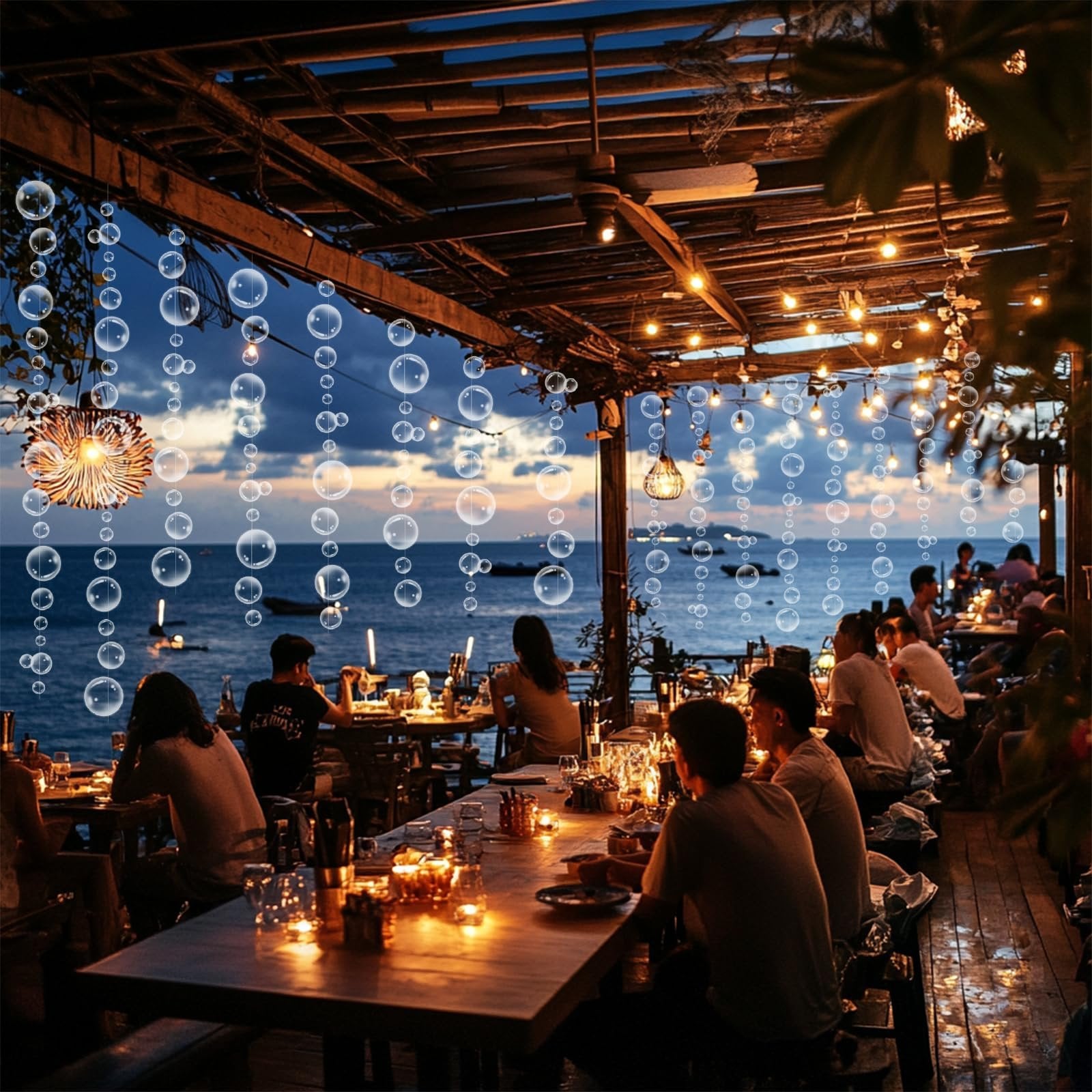 Outdoor restaurant patio with tables set for dinner, overlooking the ocean at dusk, with bubble garland decorations hanging.