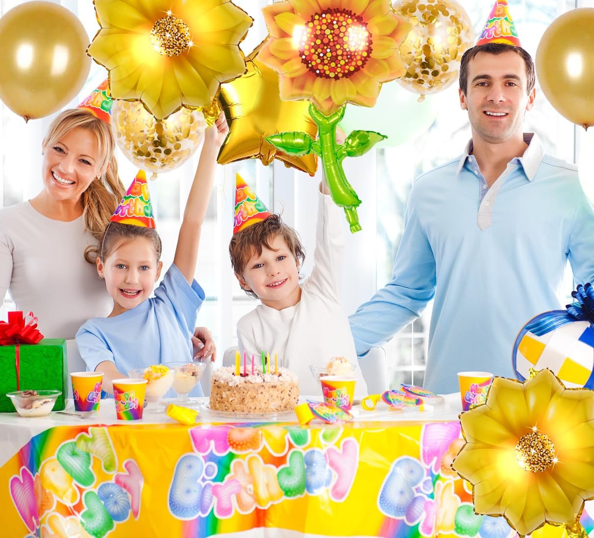 Family celebrating a birthday with sunflower and star balloons, cake, and party hats