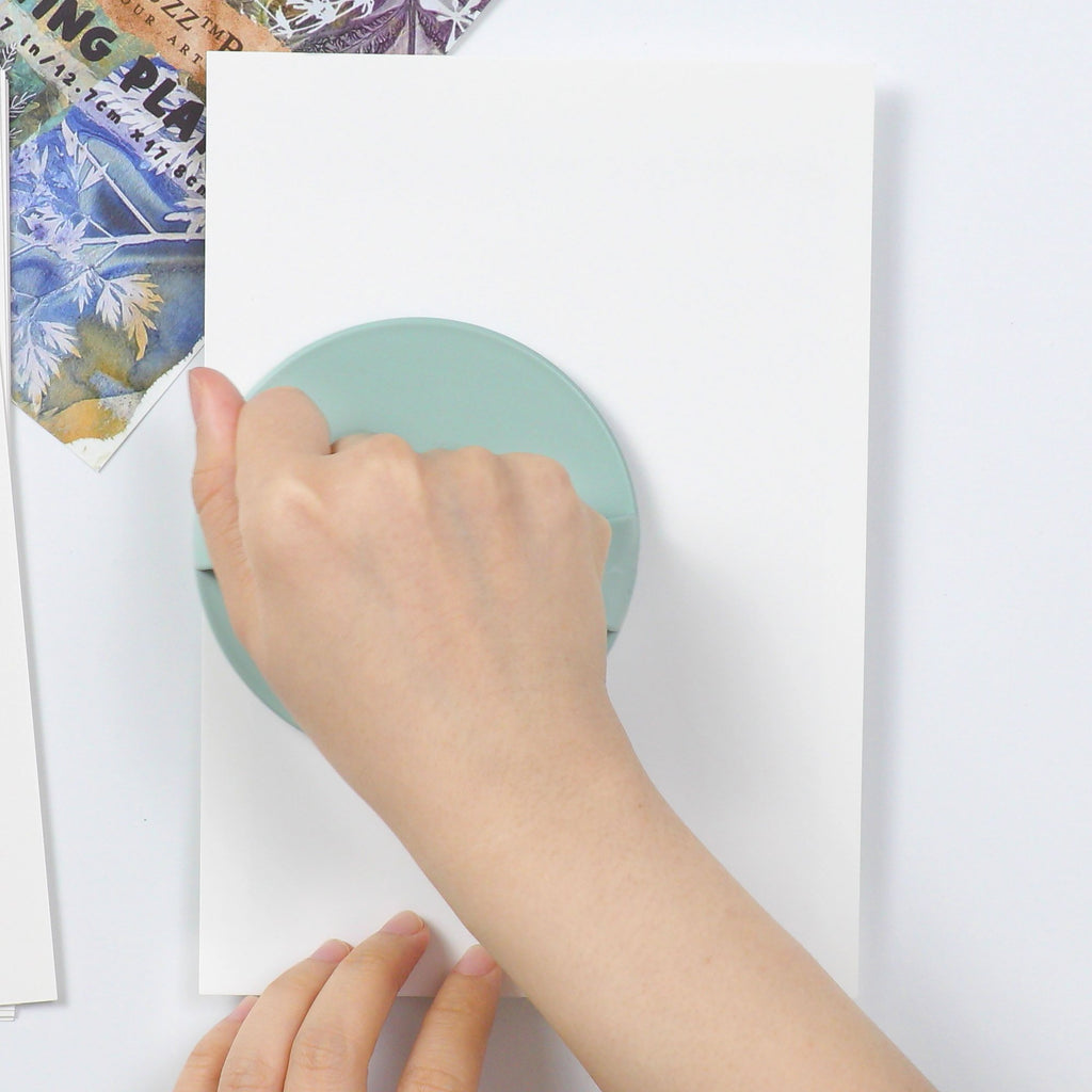 Hand using a baren tool to press paper onto a gel printing plate for art.