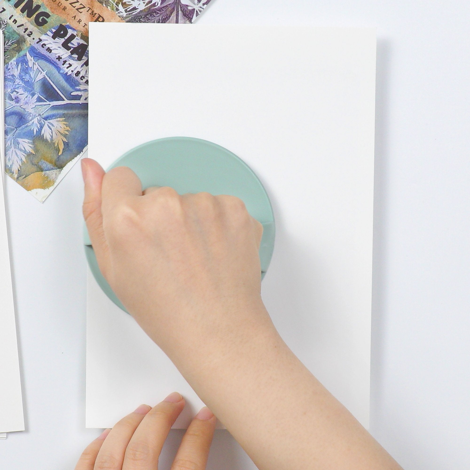 Hand using a baren tool to press paper onto a gel printing plate for art.