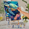 Hand painting a sea turtle on canvas with acrylic paints and brushes, surrounded by coral and fish.